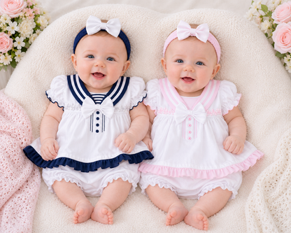 Two babies in matching outfits with bows on a soft surface.
