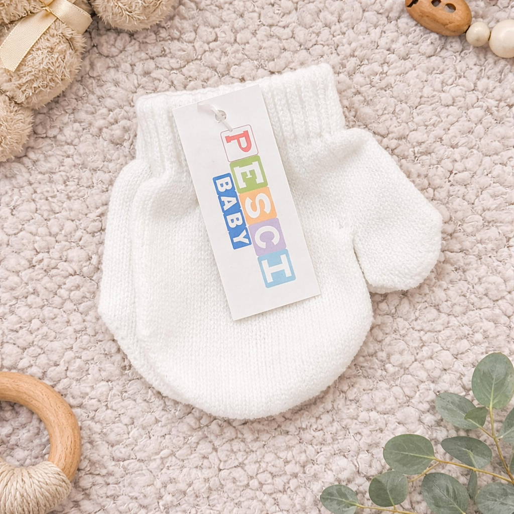 Flat lay mock up of soft white baby hand mittens displayed on a plush neutral blanket, styled with natural baby accessories including a teddy bear, wooden teether, pacifier clip, and eucalyptus leaves.