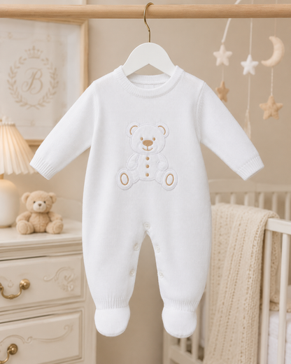 White baby onesie with teddy bear design hanging in a nursery.