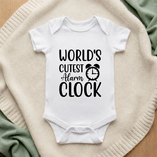 White baby onesie with 'World's Cutest Alarm Clock' text on a textured surface