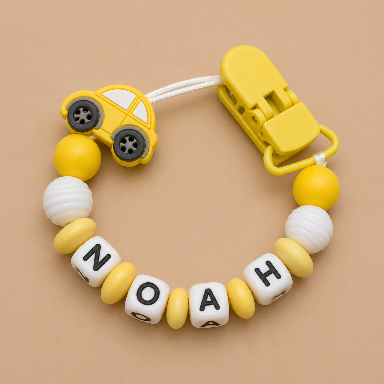 Yellow car-shaped dummy clip with 'NOAH' on a beige background