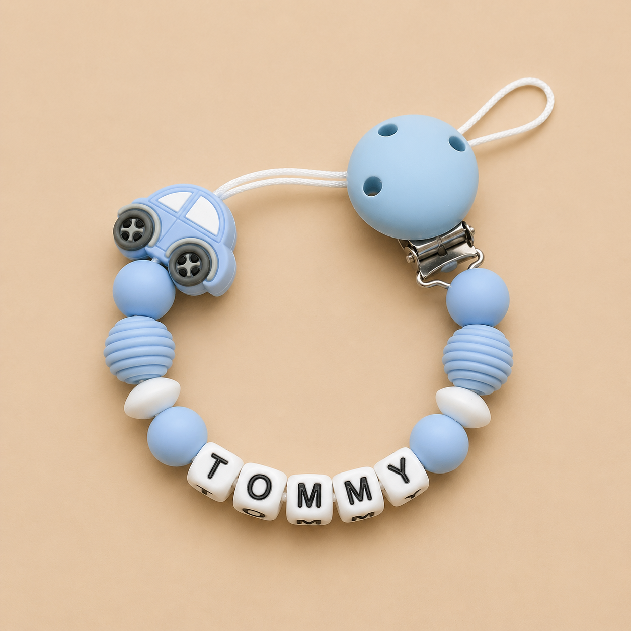Silicone pacifier clip with car charm and 'Tommy' beads on a beige background