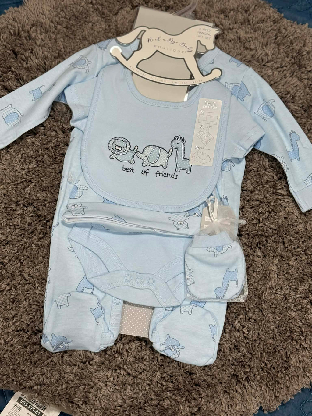 Baby clothing set with bib, pants, and blanket on a brown carpet