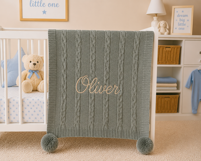 Green cable knit blanket with 'Oliver' embroidered on it in a nursery setting.