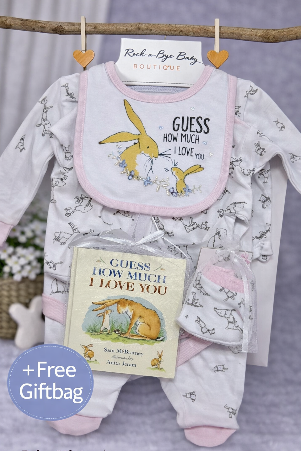 Baby gift set with bib, book, and onesie featuring 'Guess How Much I Love You' theme on a gray background.