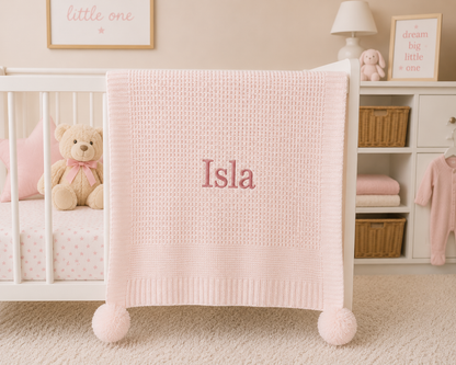 Pink baby blanket with 'Isla' embroidered on a crib in a nursery.