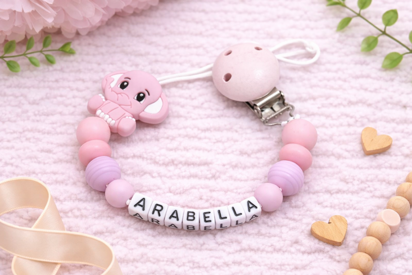 Pink and purple pacifier clip with 'ARABELLA' on a soft pink background