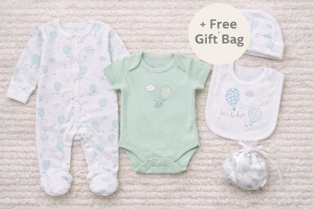 Baby clothing set with onesie, bodysuit, bib, and hat on a textured surface.