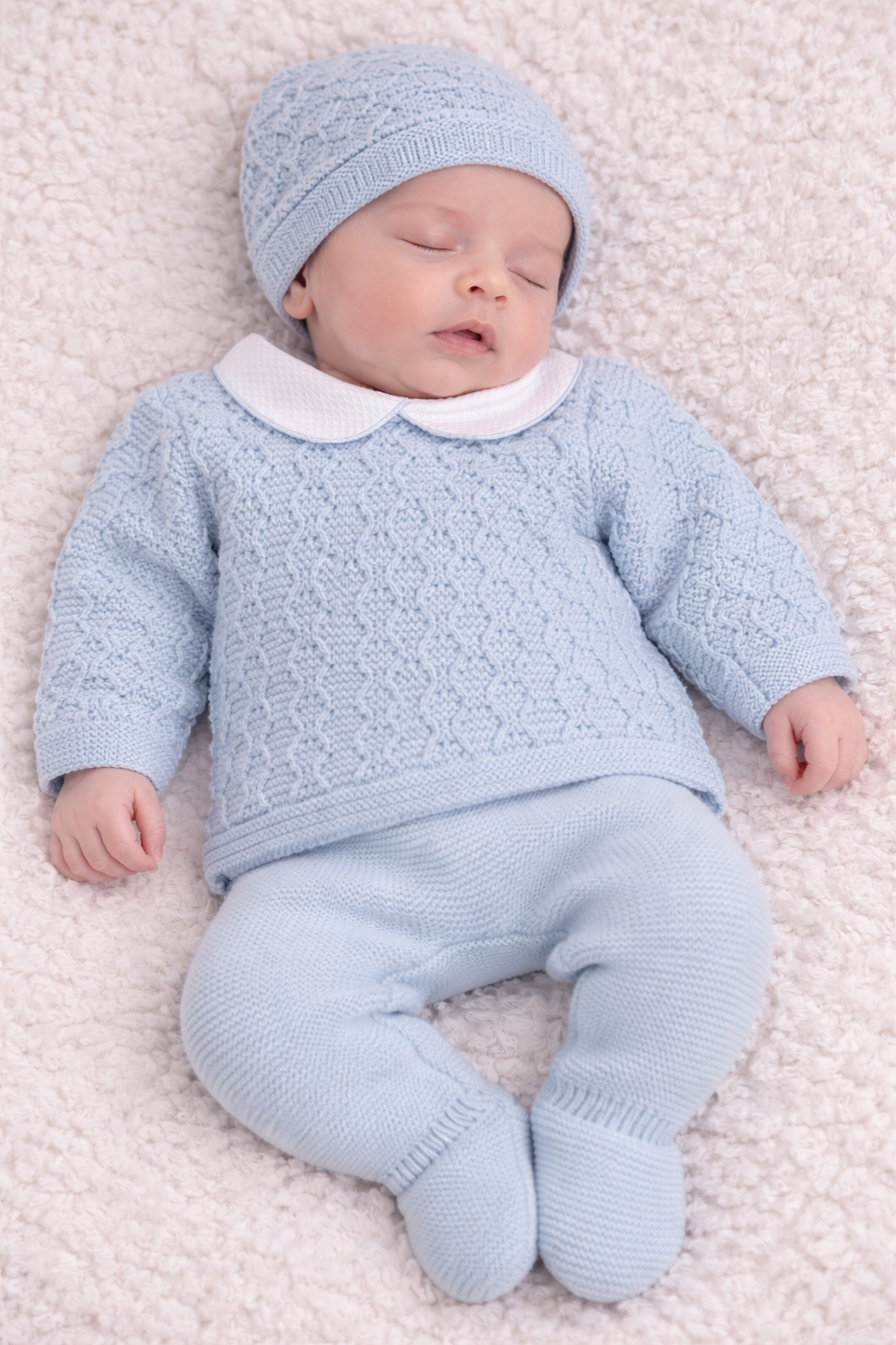 Newborn baby in a light blue knitted outfit lying on a soft surface