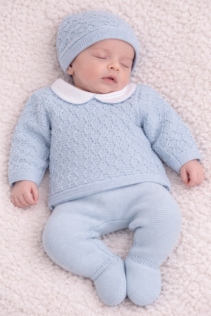 Newborn baby in a light blue knitted outfit lying on a soft surface