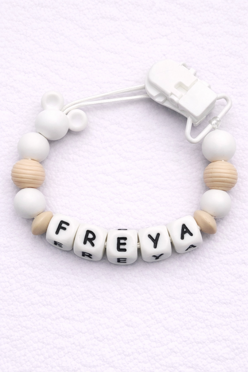 dummy clip with letter beads spelling 'FREYA' on a light purple background