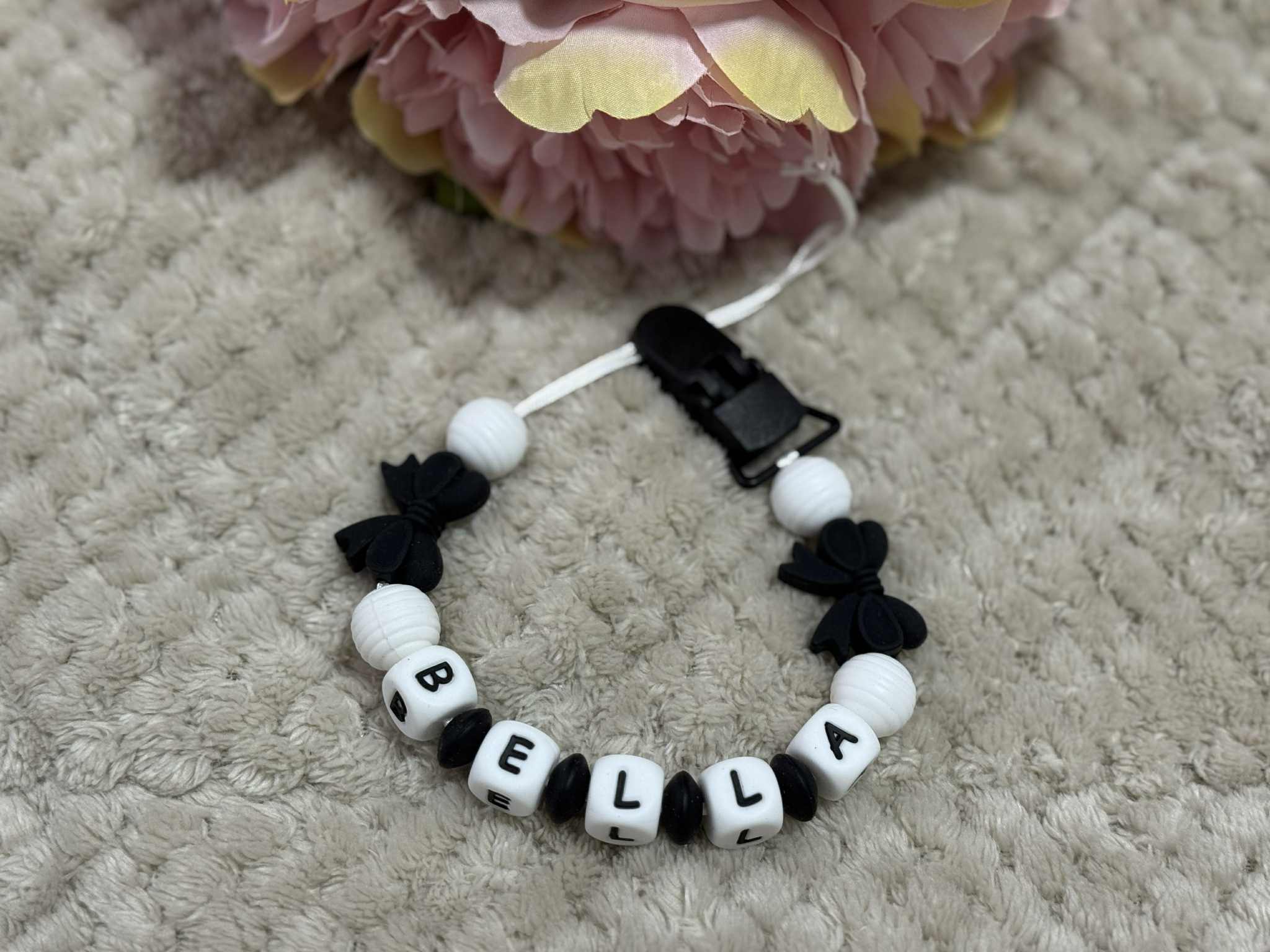 Dummy Chain with 'BELLA' beads on a textured surface with flowers in the background