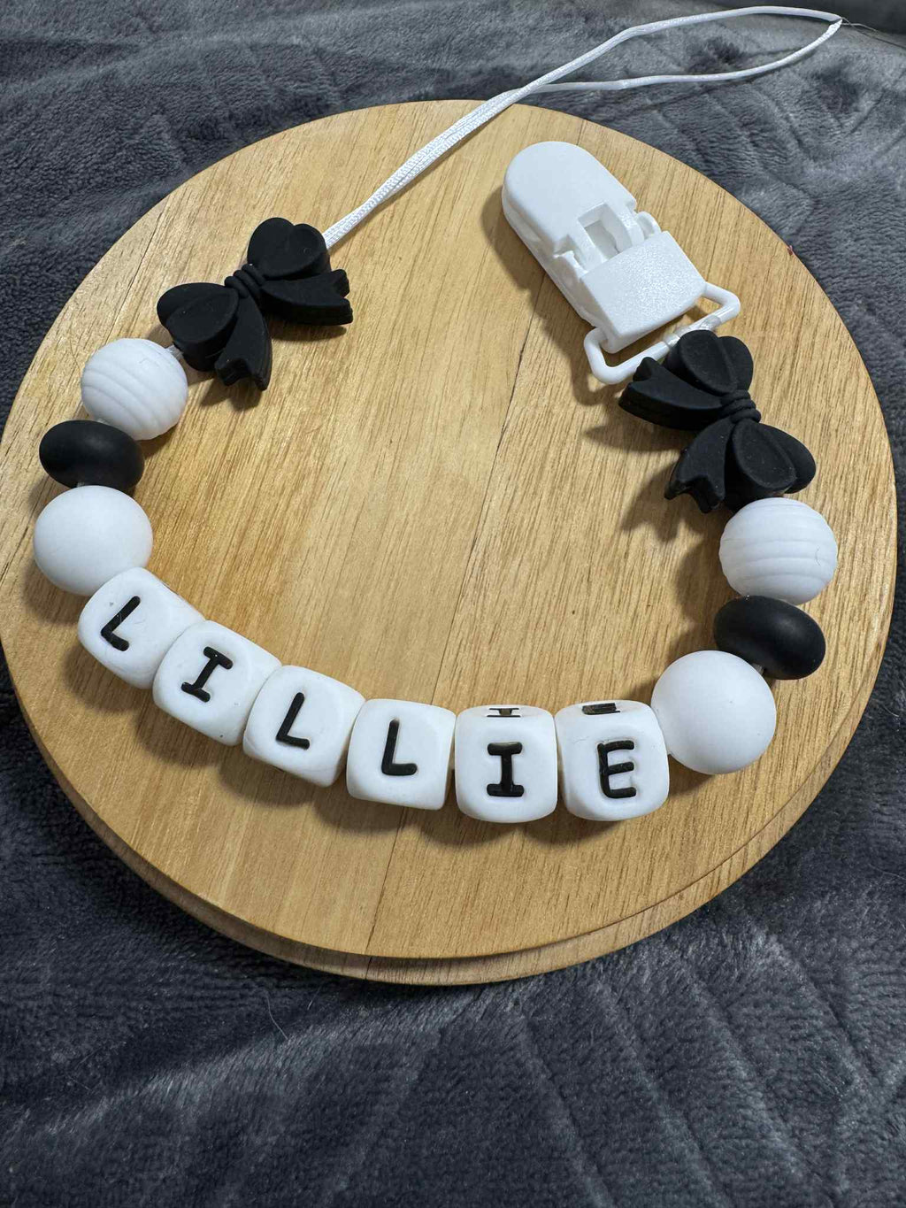 Dummy Chain with black bows and white beads spelling 'LILLIE' on a wooden board.