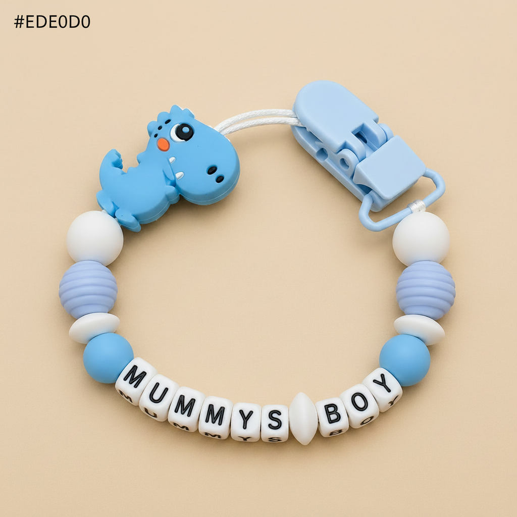 dummy clip with blue dino design and 'MUMMYS BOY' letter beads on a beige background