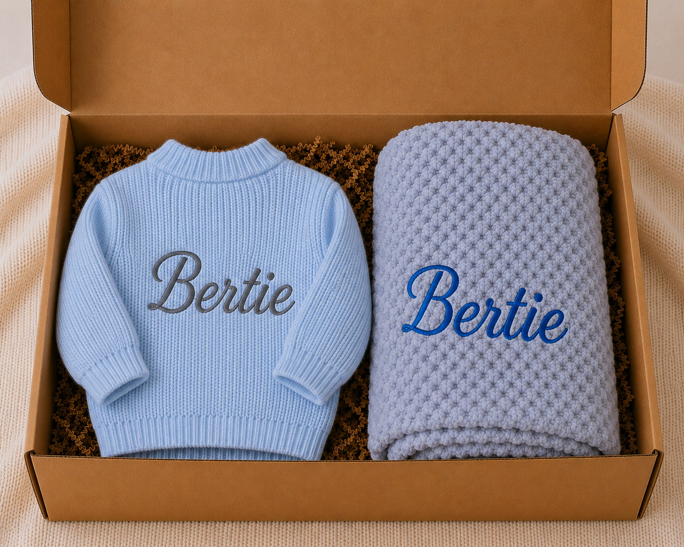Blue baby sweater and blanket with 'Bertie' embroidery in a cardboard box.