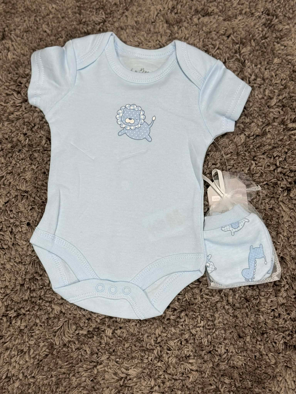 Baby blue onesie with lion design and matching hat on a brown carpet