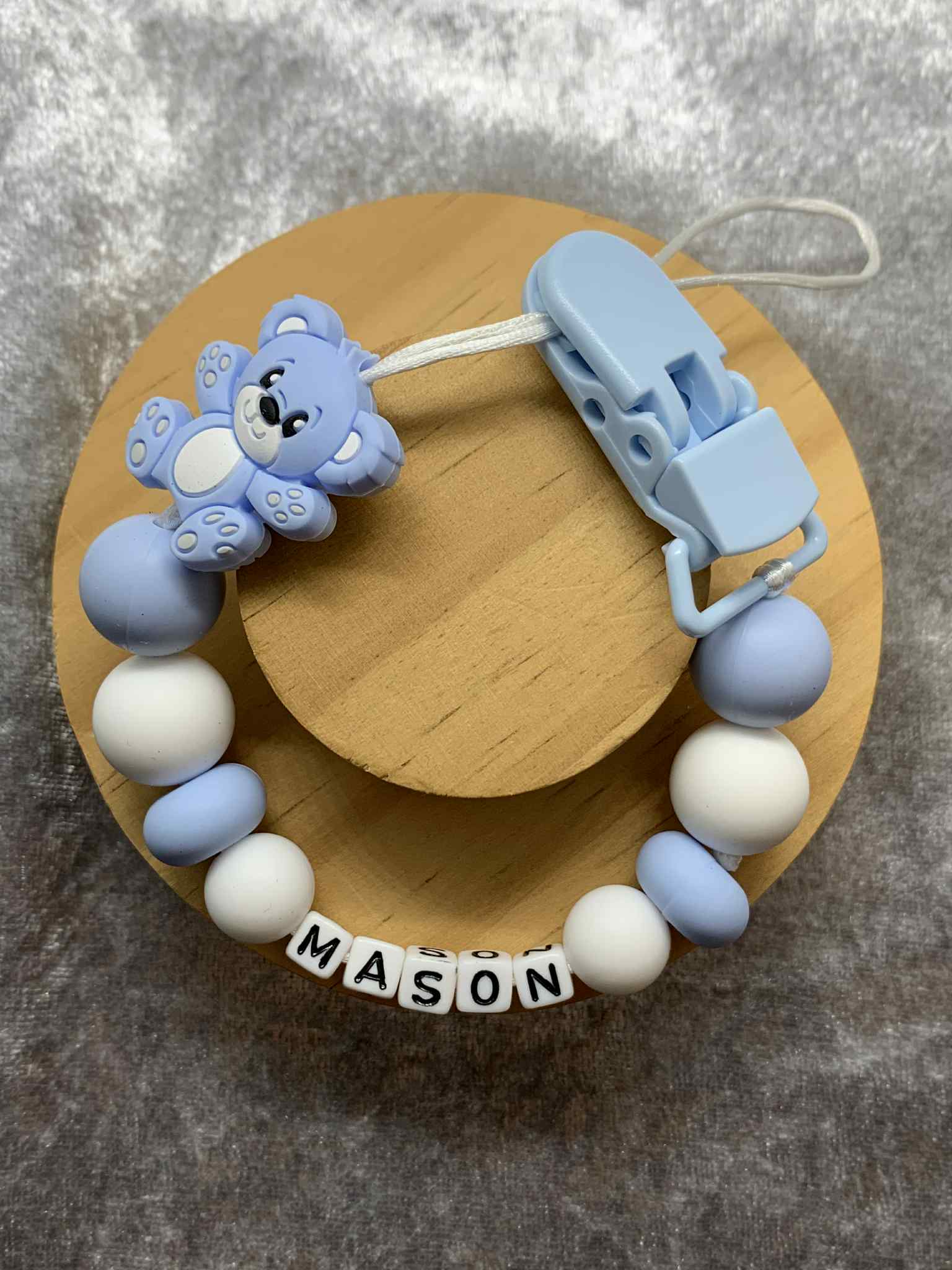 Baby teether with blue and white beads and a teddybear charm on a wooden base. Personalised.