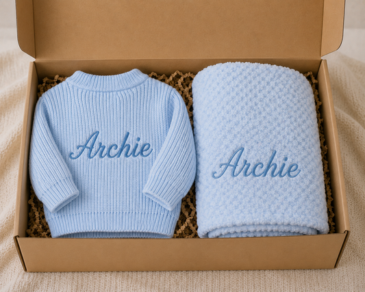 Blue baby sweater and blanket set with 'Archie' embroidery in a cardboard box.