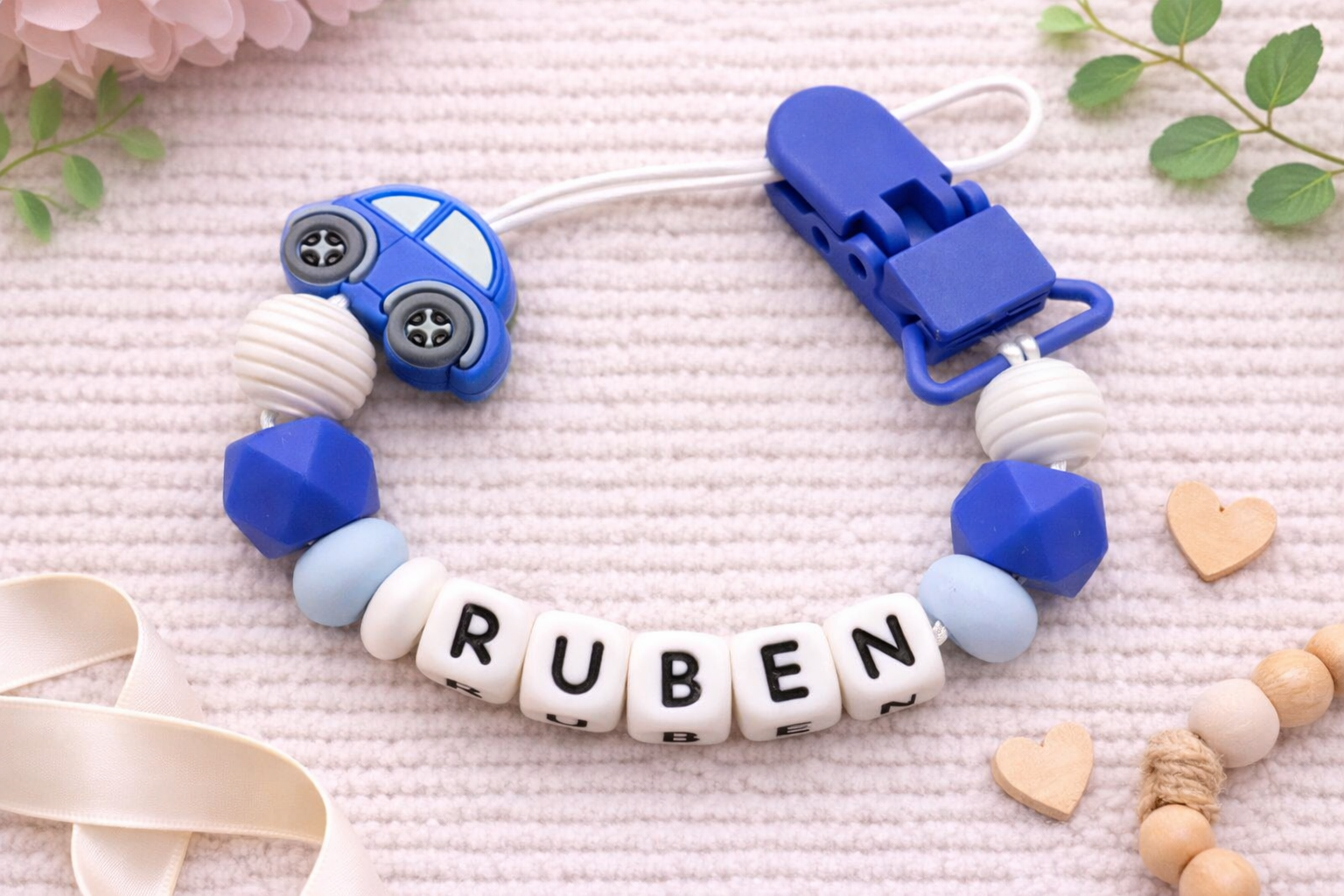 personalised dummy clip with blue car charm and 'RUBEN' beads on a pink background