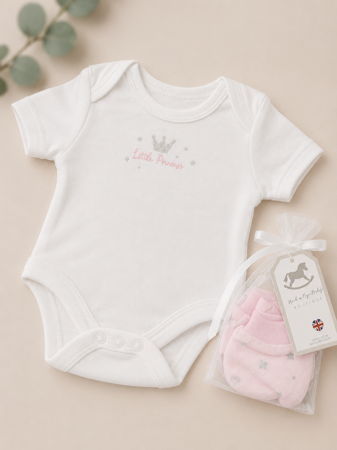 White baby bodysuit with 'Little Princess' text and pink baby booties on a beige background