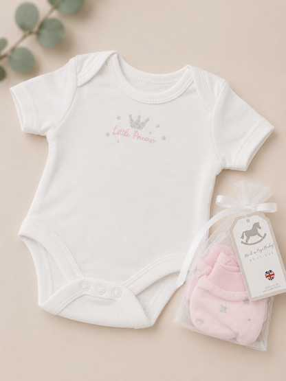 White baby bodysuit with 'Little Princess' text and pink baby booties on a beige background