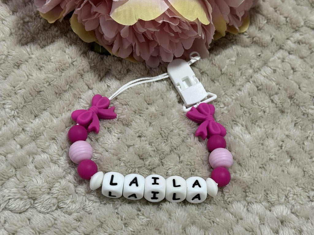 Dummy Chain with pink and white beads spelling 'LAILA' on a textured surface with flowers in the background.