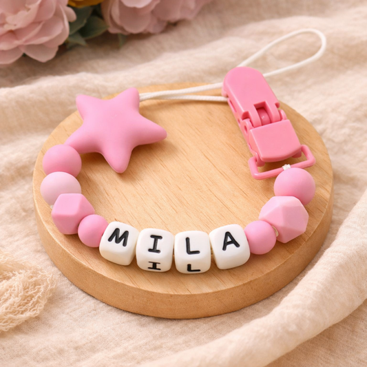 Pink baby teether with 'MILA' name beads on a wooden base