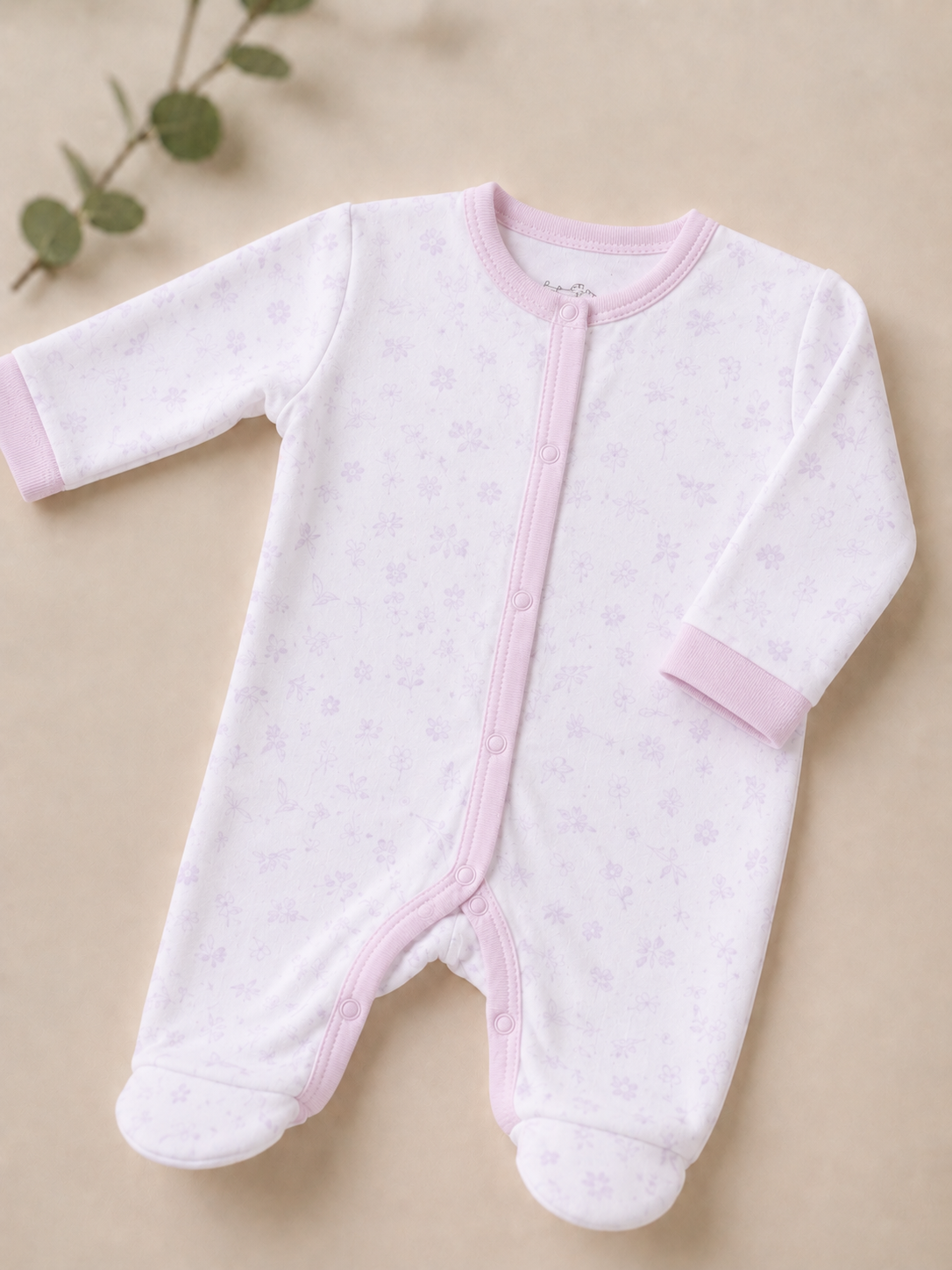 White baby onesie with pink accents on a beige background