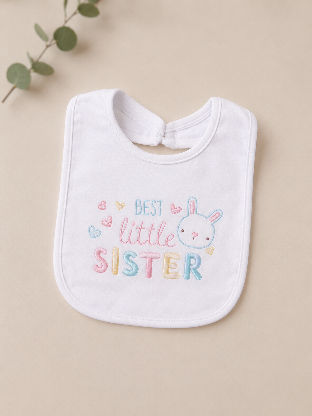 White bib with 'Best Little Sister' text and bunny illustration on a beige background