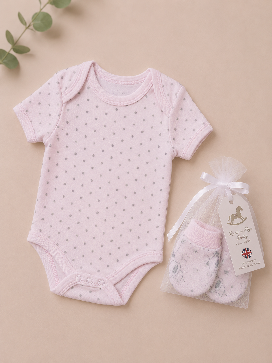 Pink baby bodysuit with star pattern and matching mittens on a beige background