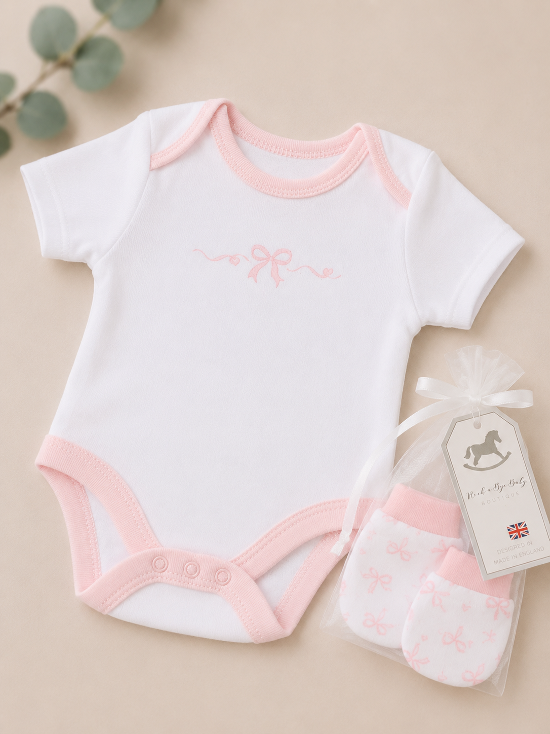 Baby bodysuit and mittens set with pink accents on a beige background