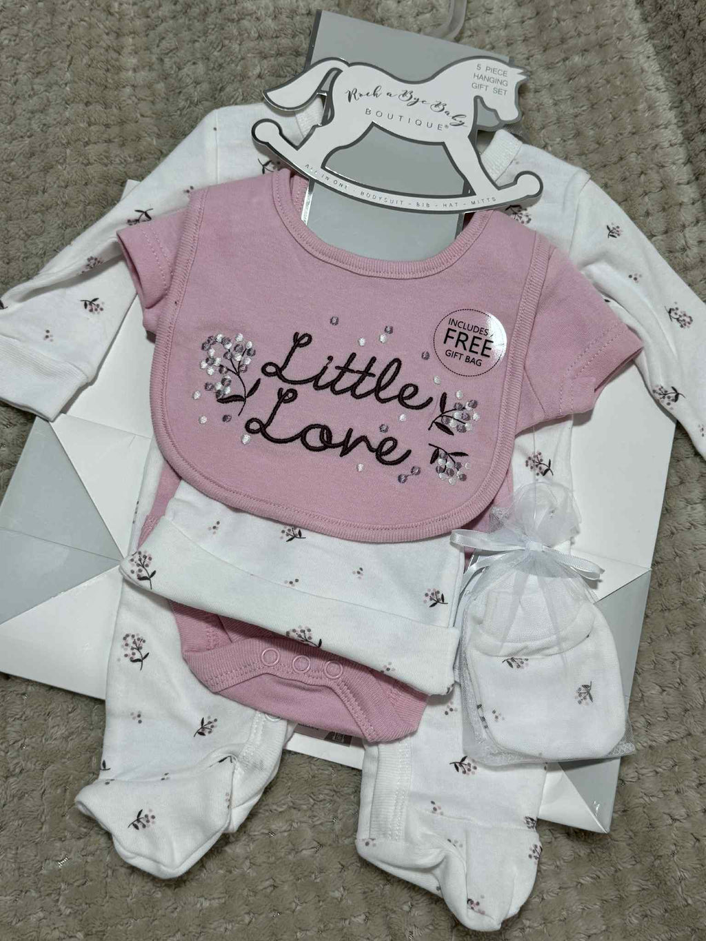 Baby clothing set with pink bib, onesie, and hat on a gray surface