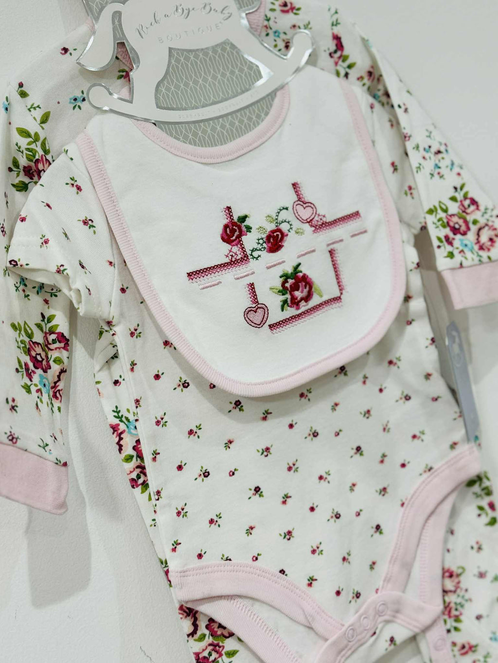 Baby clothing set with floral patterns and embroidered designs on a white background