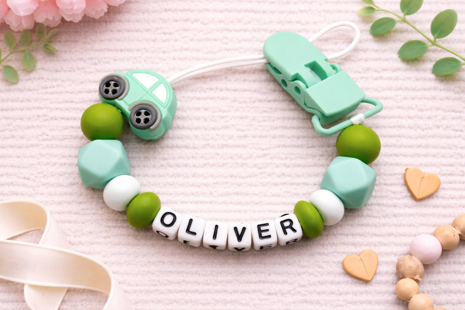 green soother holder for baby boy with green and white beads and a clip on a pink background