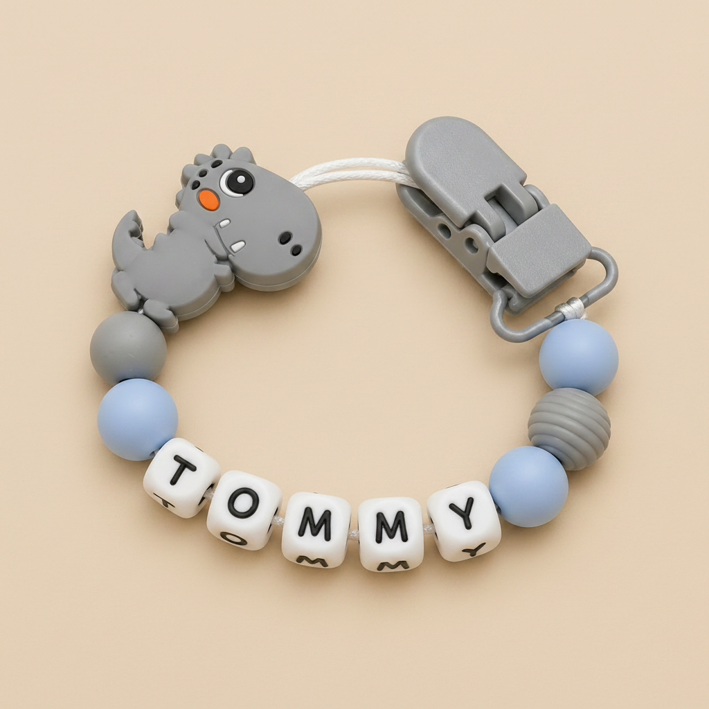 dummy clip with dinosaur design and 'TOMMY' name on a beige background