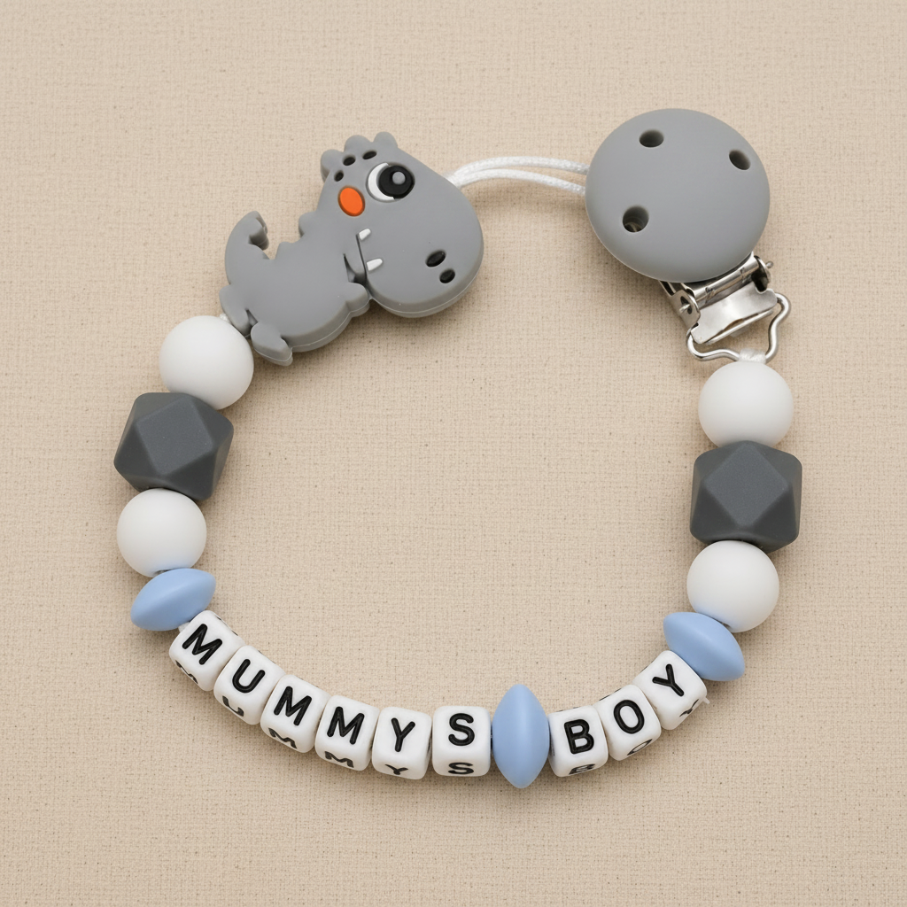dummy clip with dinosaur charm and 'Mummy's Boy' beads on a beige background