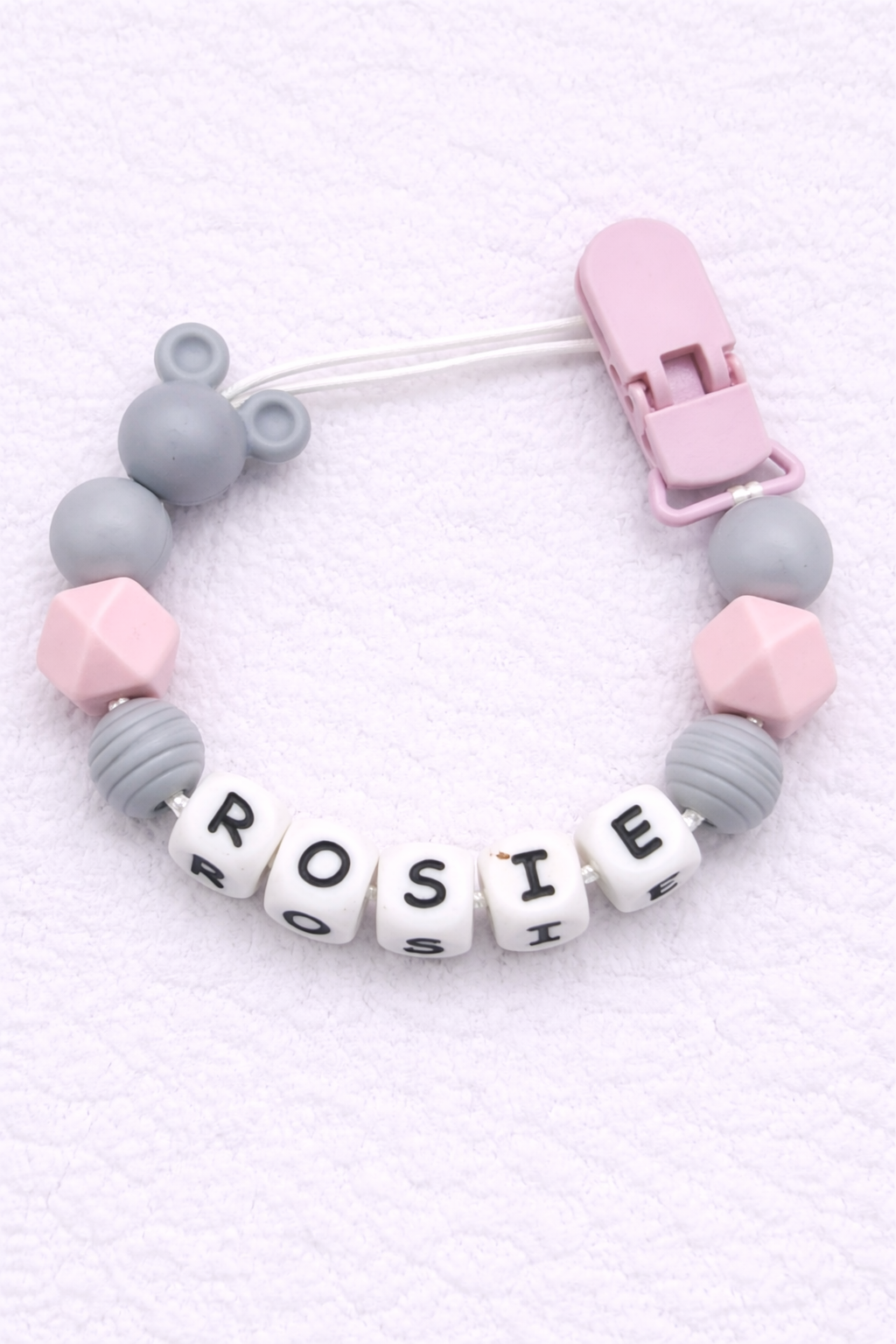 dummy clip with letter beads spelling 'ROSIE' on a light pink background