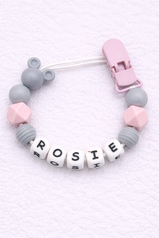 dummy clip with letter beads spelling 'ROSIE' on a light pink background