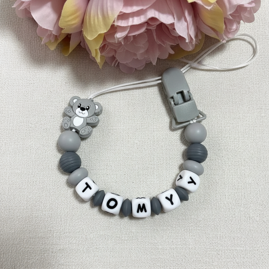 Personalised grey teddy bear dummy clip on a soft white luxury linen textured background.