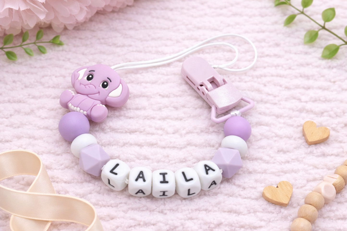 Purple baby dummy clip with 'LAILA' beads on a pink background