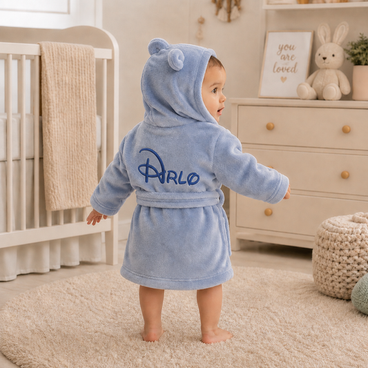 Baby in a blue robe with 'arlo' branding standing in a nursery.