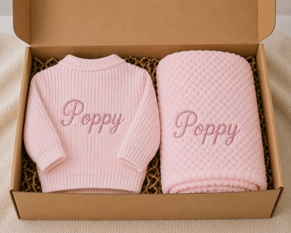 Pink baby sweater and blanket set with 'Poppy' embroidery in a cardboard box.