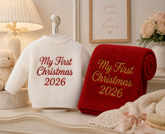 White sweater and red blanket with 'My First Christmas 2026' text on a decorative surface.