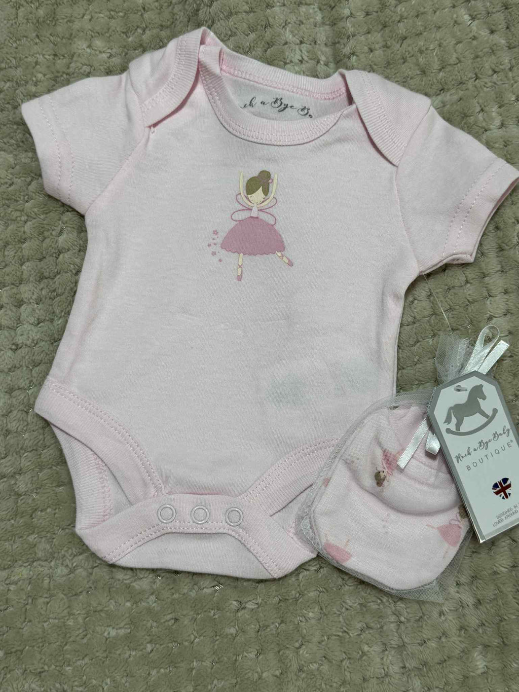 Baby onesie with a fairy design and matching hat on a textured surface