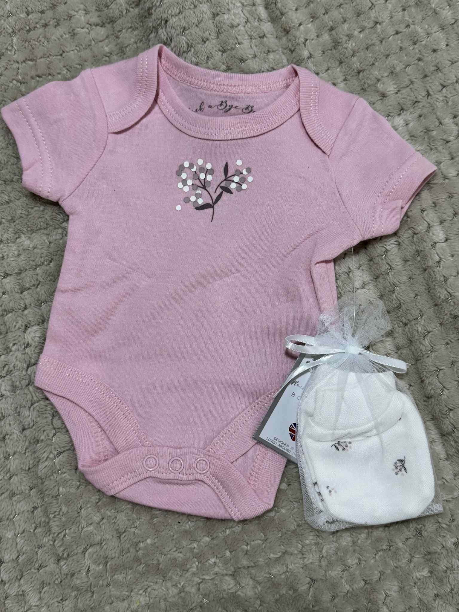 Pink baby bodysuit with floral design and white hat on a textured surface