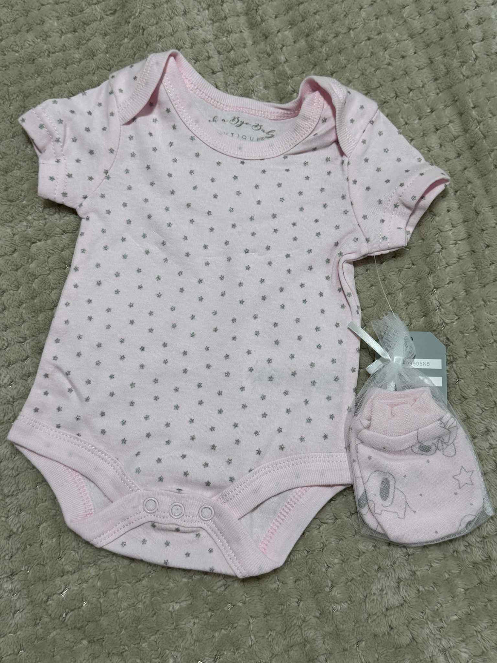 Baby bodysuit with pink trim and matching booties on a textured surface