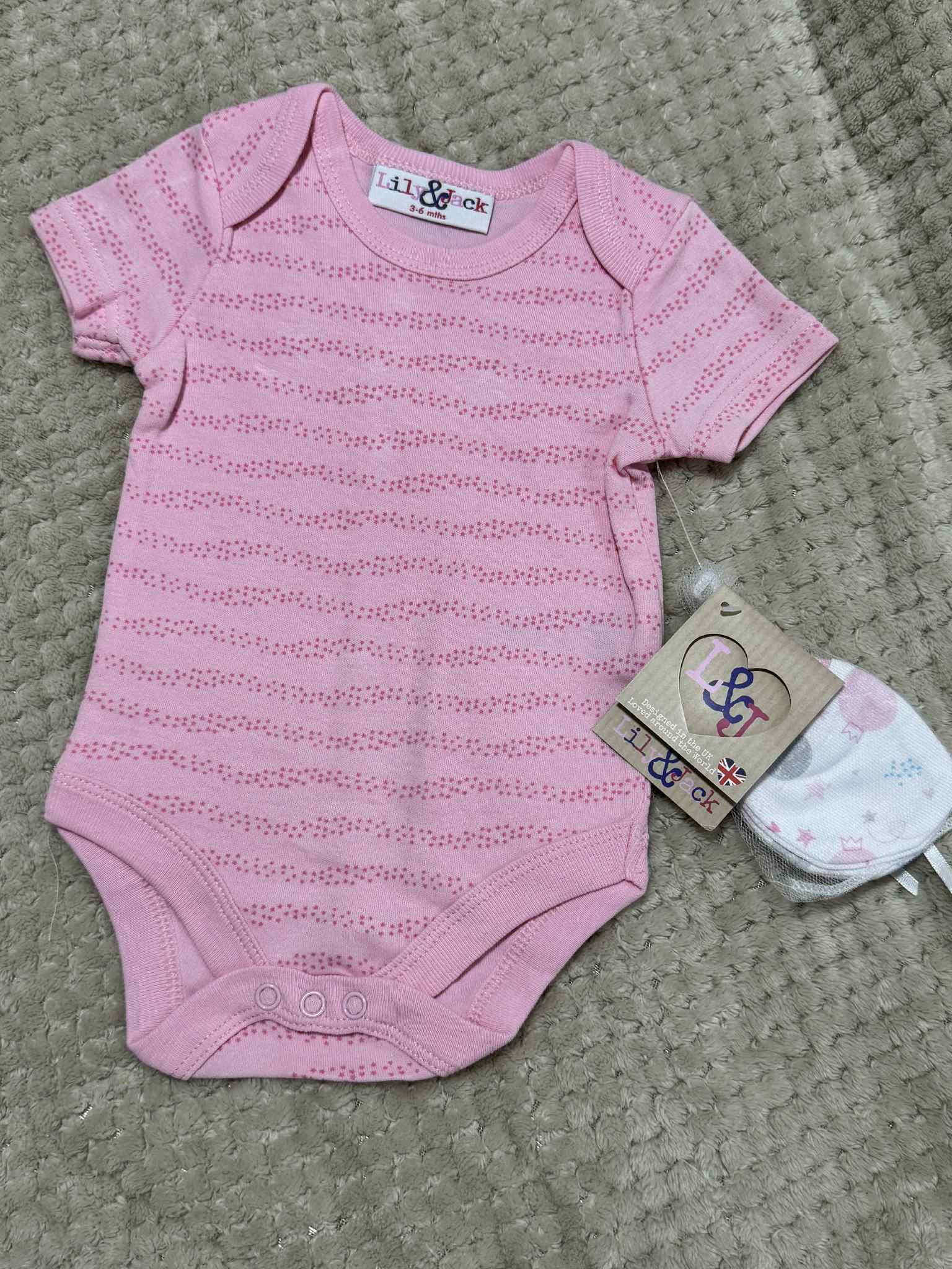 Pink baby onesie with matching hat on a textured surface