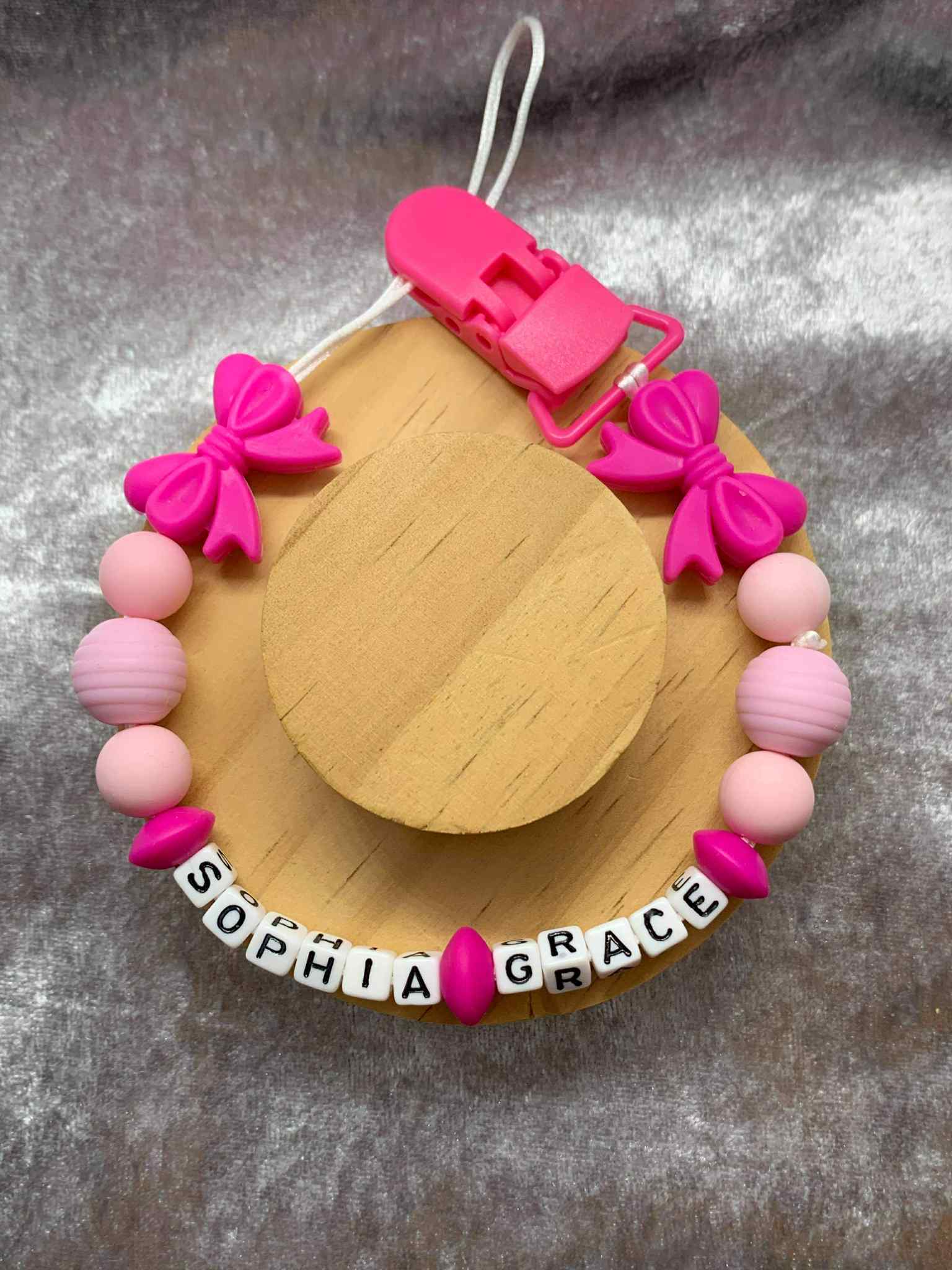 dummy clip for baby girls with pink and purple decorative elements on a gray background