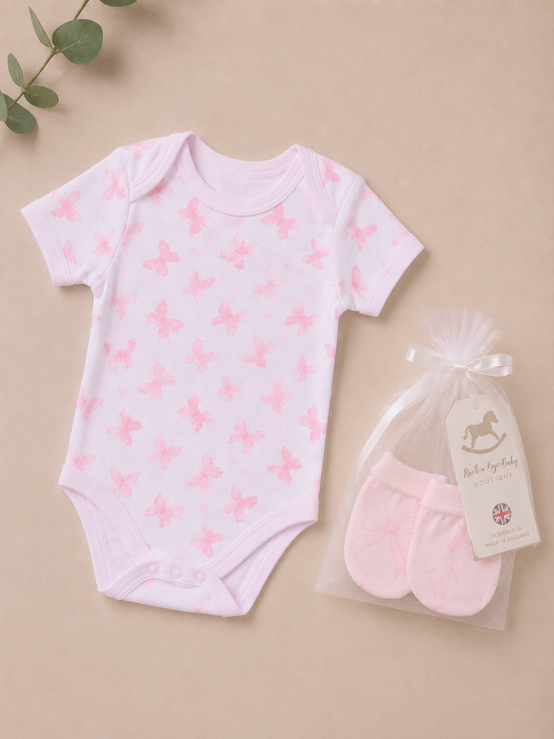 Baby onesie with pink butterfly pattern and matching socks on a beige background