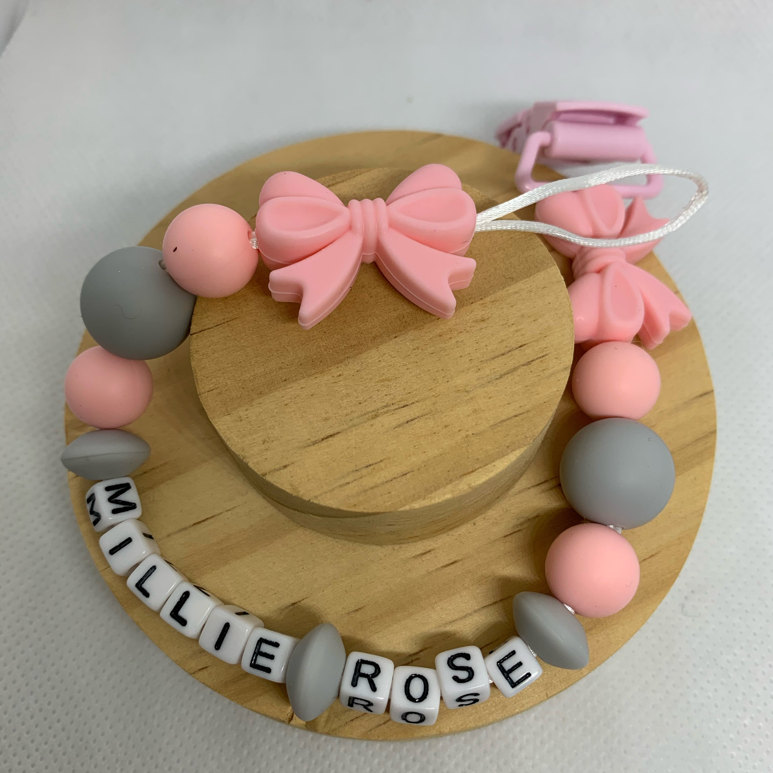pink dummy clip with pink bows and colorful beads on a wooden stand.